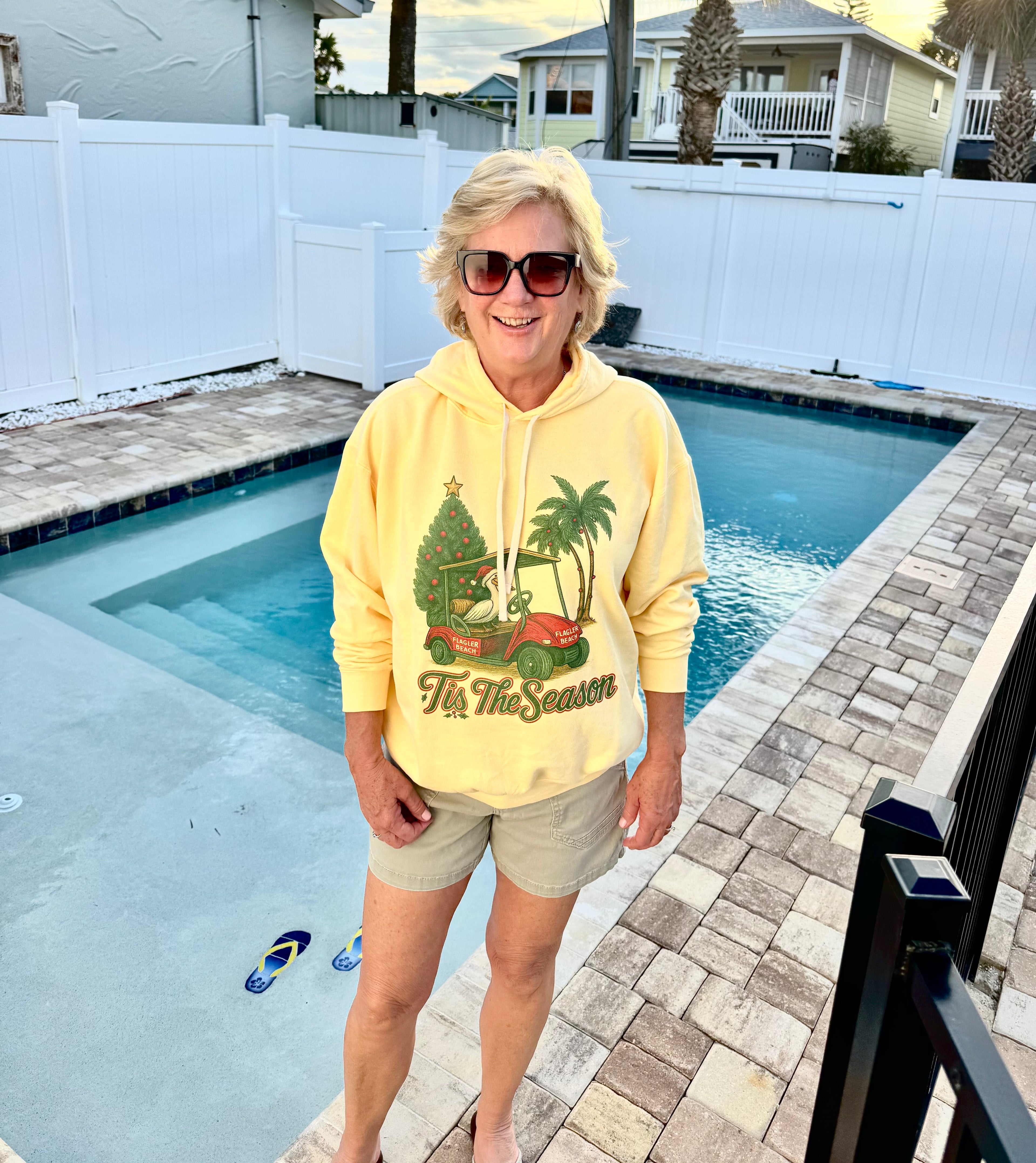 Person wearing a yellow Flagler Beach hoodie with a graphic design, standing by a pool.

